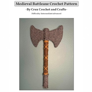 May include: A crochet pattern titled Medieval Battleaxe Crochet Pattern by Crux Crochet and Crafts with an intermediate/advanced difficulty level. The image shows a double-headed battleaxe made of grey and brown yarn with a crisscross pattern.