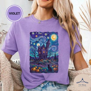 Puede incluir: Una camiseta violeta con un estampado gráfico de una casa encantada bajo un cielo estrellado y arremolinado. El diseño incluye una luna creciente, árboles desnudos, un gato negro y calabazas naranjas. El texto VIOLET aparece en un círculo.