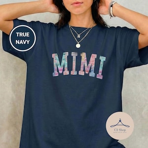 Puede incluir: Camiseta azul marino con la palabra "MIMI" en una fuente colorida de estilo acuarela. La camiseta también presenta el texto "TRUE NAVY" en un círculo blanco y un logotipo de C2 Shop.