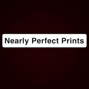 May include: A rectangular white label centered against a solid black background. The text "Nearly Perfect Prints" is printed in a clear, bold, black sans-serif font on the white label, occupying the center of the composition.
