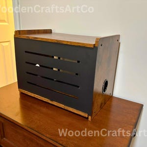 May include: A wooden box with a dark brown finish and a black front panel featuring horizontal slots. The top and sides of the box have a lighter wood tone. The text "WoodenCraftsArtCo" is visible in the image.