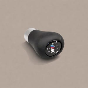 May include: Black leather gear stick knob with a silver base. The knob displays the BMW M logo and gear shift pattern: R, 1, 2, 3, 4, and 5. Designed for a car's manual transmission.