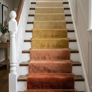 May include: A staircase with a gradient carpet in shades of beige, yellow, and rust. The carpeted steps are secured with brass rods. The stairs have white risers and dark wood treads and handrails.