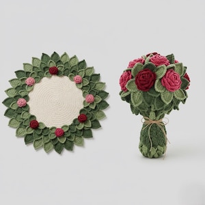 Op de afbeelding: Gehaakte krans en boeket rozen. De krans heeft groene bladeren met een crèmekleurig midden en is versierd met rode en roze rozen. Het boeket heeft rode en roze rozen omgeven door groene bladeren, vastgebonden met touw.