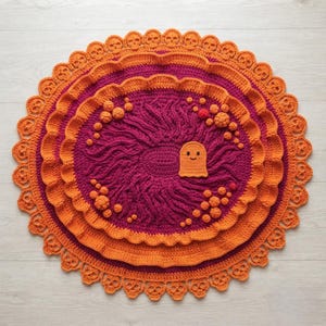 May include: A round, multi-layered crochet rug featuring a deep magenta center with textured, swirling yarn patterns and small raised spheres. The rug is bordered by vibrant orange ruffled layers and an outer edge detailed with skull motifs.