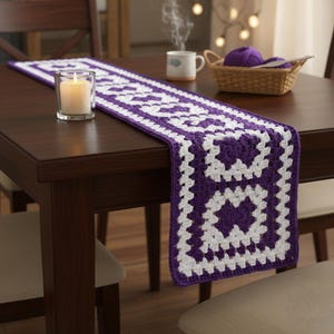 May include: A handmade, purple and white crochet table runner with a geometric pattern. The runner is placed on a dark brown wooden table. A lit candle in a glass holder, a cup of coffee, and a basket with yarn are also on the table.