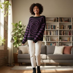 Puede incluir: Un suéter negro y morado con un diseño de espiral. El suéter tiene cuello redondo y mangas largas. La modelo lleva pantalones blancos y botas negras. El fondo incluye un sofá, una estantería y plantas.