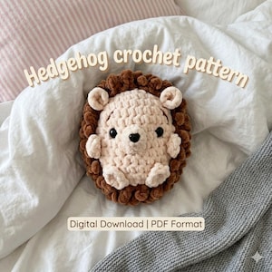 May include: A handmade crochet hedgehog plush toy with a cream-colored face and dark brown textured quills, featuring black safety eyes and a small black nose. The text "Hedgehog crochet pattern" and "Digital Download | PDF Format" is visible.