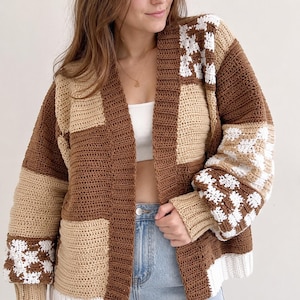 May include: A long-sleeve crochet cardigan featuring a patchwork design in shades of brown, beige, and white. The garment includes solid color blocks and checkered patterns, with a ribbed collar, cuffs, and hem, worn over a white top and blue jeans.
