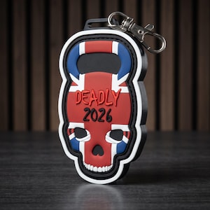 May include: A rubberized keychain shaped like a skull with a kettlebell handle, featuring a red, white, and blue Union Jack pattern. The text "DEADLY" is printed in red above the black numbers "2026" on the front of the skull-shaped design.