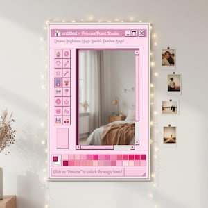 Könnte beinhalten: Ein gerahmtes rosa Kunstwerk mit dem Titel "untitled - Princess Paint Studio" im Design einer Computerschnittstelle. Der Text enthält "Dreams Brightness Magic Sparkle Rainbow Angel" und "Click on 'Princess' to unlock the magic hints!". Das Kunstwerk hängt an einer weißen Wand mit Lichterketten und Fotos.