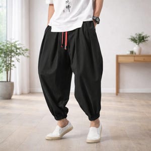May include: Black harem pants with a relaxed fit, featuring a red drawstring at the waist and elastic cuffs. The pants are paired with white slip-on shoes and a white t-shirt. The overall style is casual and comfortable.