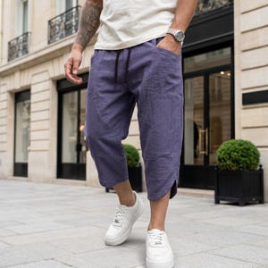 May include: Purple cropped trousers featuring a drawstring waistband, side pockets, and a relaxed fit. The pants have a straight-leg cut that ends mid-calf, showcasing a solid color design with visible stitching details along the side seams.
