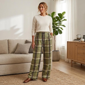 May include: A woman wearing a cream-colored sweater and green plaid wide-leg pants. The pants feature a classic plaid pattern in shades of green, black, and white. She is wearing brown leather loafers. The outfit is suitable for casual or business casual wear.