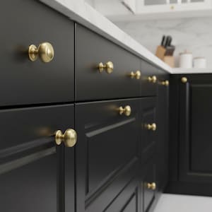 May include: Close-up of black kitchen cabinets with gold-colored knobs. The knobs are round and have a simple, elegant design. The cabinets are clean and modern, with a white countertop in the background. The overall aesthetic is sleek and stylish.