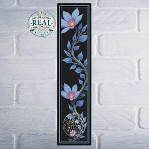 Puede incluir: Un marcapáginas rectangular vertical con fondo negro y una enredadera de flores y hojas de color azul claro. El diseño incluye un logotipo circular en la parte inferior con el texto EL REINO DE LOS HILOS MÁGICOS y un icono de corona.