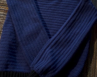 May include: A navy blue sweater with long sleeves. The sweater has a ribbed texture on the sleeves and a solid knit body. The cuffs and hem are black. The sweater is folded on a patterned surface.