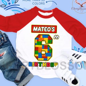 May include: A white and red raglan-style birthday shirt with the name "Mateo's" and the number "6" in a colorful block design. The words "Birthday" are below the number. Includes blue jeans and white sneakers.