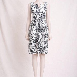 Peut inclure: Une robe sans manches arrivant au genou, dotée d'une base blanche ornée d'un motif floral et végétal noir contrasté. Le vêtement présente une encolure échancrée, un corsage ajusté et une jupe à plis discrets pour une silhouette structurée.