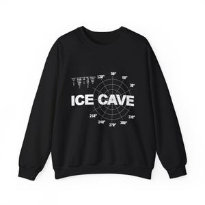 May include: A black long-sleeve sweatshirt featuring a white graphic print on the chest. The design includes a circular radar-style grid with degree markings and the text ICE CAVE in large capital letters, along with smaller technical data text.