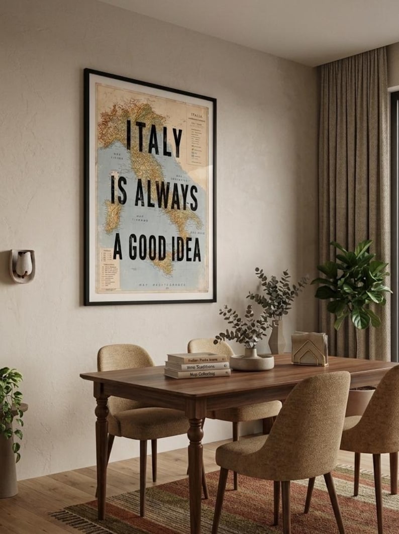 May include: Framed wall art with the text "ITALY IS ALWAYS A GOOD IDEA" over a vintage map of Italy. The artwork hangs above a wooden dining table with chairs, books, and decorative items.