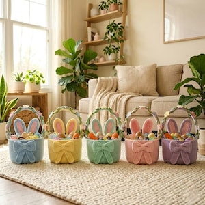 May include: Five pastel-colored Easter baskets with bunny ears and bow accents. The baskets are filled with colorful eggs and carrots. The baskets are blue, yellow, green, pink, and purple. The baskets are sitting on a beige rug.