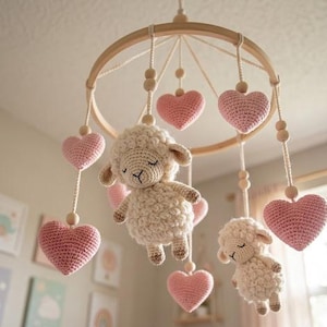 Può includere: Mobile per bambini fatto a mano con due pecorelle all'uncinetto e diversi cuori rosa sospesi a un cerchio di legno. Le pecorelle sono bianco sporco con gli occhi chiusi e i cuori sono rosa tenue.