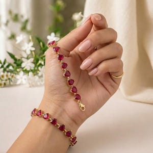 May include: A gold-toned bracelet featuring a series of triangular-cut deep red gemstones linked together. The bracelet is displayed in a chain-like arrangement with a lobster claw clasp visible at the end of the gemstone strand.