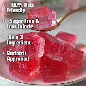 May include: A close-up of several red, cube-shaped gelatin desserts on a pink plate, with one being held on a gold spoon. The image includes text that reads "100% Keto-Friendly", "Sugar-Free & Low Calorie", "Only 3 Ingredient", and "Bariatric Approved".