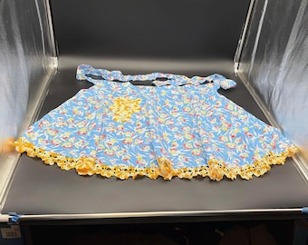 Delantal corto vintage azul con estampado floral, ribete de ganchillo amarillo y bolsillo.
