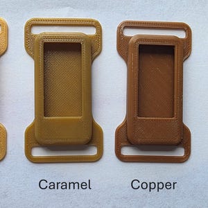 May include: Four 3D-printed plastic buckles in gold, caramel, copper, and brown. Each buckle has a rectangular frame with a smaller, inset rectangle and two loops. The colors are labeled below each buckle.