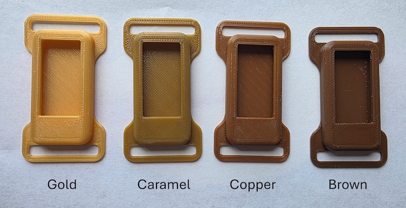 May include: Four 3D-printed plastic buckles in gold, caramel, copper, and brown. Each buckle has a rectangular frame with a smaller, inset rectangle and two loops. The colors are labeled below each buckle.