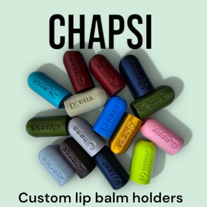 Könnte beinhalten: Eine Sammlung farbenfroher Lippenbalsamhalter in verschiedenen Farbtönen, darunter Blau, Grün, Rosa und Gold. Jeder Halter ist mit einem eindeutigen Namen versehen. Das Wort "CHAPSI" steht oben, darunter "Custom lip balm holders".