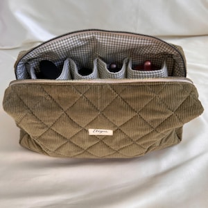 May include: Olive green quilted corduroy makeup bag with a gingham interior and multiple compartments. The bag has a zipper closure and a small label that reads "Elviva".