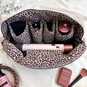 Peut inclure: Trousse de maquillage en velours c&ocirc;tel&eacute; beige avec int&eacute;rieur imprim&eacute; l&eacute;opard. Elle contient des outils de beaut&eacute;, dont un s&egrave;che-cheveux Dyson, une brosse &agrave; cheveux et du blush. Le sac est ouvert.