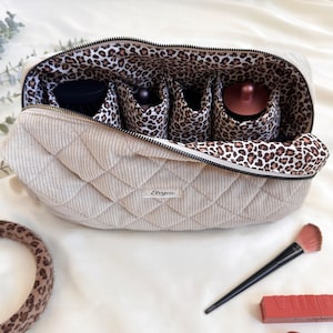 Peut inclure: Une trousse de maquillage beige en velours c&ocirc;tel&eacute; matelass&eacute; avec un int&eacute;rieur &agrave; imprim&eacute; l&eacute;opard. Le sac est dot&eacute; d'une fermeture &eacute;clair et de plusieurs compartiments pour organiser les cosm&eacute;tiques. Un pinceau de maquillage et du rouge &agrave; l&egrave;vres sont visibles.
