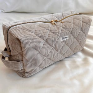 Peut inclure: Une trousse de maquillage en velours c&ocirc;tel&eacute; beige avec un motif losange matelass&eacute;. Le sac a une fermeture &eacute;clair dor&eacute;e et une petite &eacute;tiquette avec du texte. Le sac est de forme rectangulaire avec une poign&eacute;e sur le c&ocirc;t&eacute;.