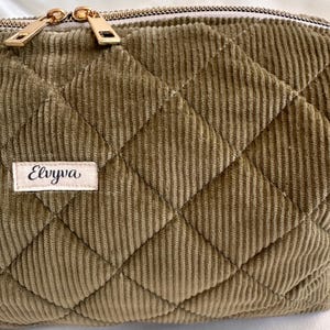 May include: Close-up of a quilted corduroy pouch in a muted olive green color. The pouch features a diamond pattern and a gold zipper. A small label with the name "Elvyva" is sewn on the front.