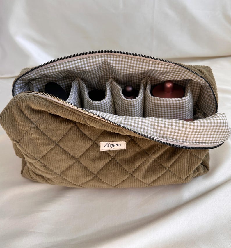 May include: Open olive green quilted corduroy cosmetic bag with a gingham lining and interior compartments. The bag has a zipper closure and a small label that reads "Elvya".