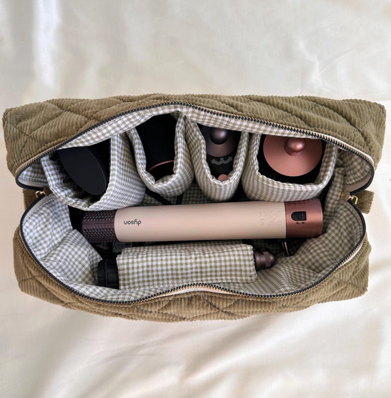 May include: Olive green quilted corduroy cosmetic bag with a zipper closure. The interior features multiple compartments lined with a gray and white gingham pattern. The bag contains hair styling tools, including a Dyson hair styler.