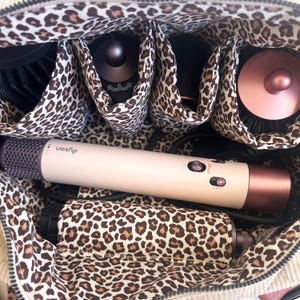 Peut inclure: Une trousse de voyage beige et l&eacute;opard contenant des outils de coiffure. On aper&ccedil;oit un s&egrave;che-cheveux Dyson et divers accessoires. L'int&eacute;rieur pr&eacute;sente un motif l&eacute;opard avec plusieurs compartiments pour l'organisation.