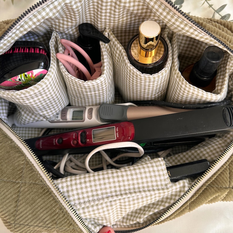 May include: A sage green corduroy cosmetic bag with a gingham lining, filled with beauty tools and products. Items include a hairbrush, hair ties, perfume, hair straightener, and other styling tools. The bag has a zipper closure.