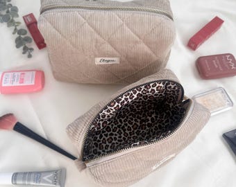 Peut inclure: Deux trousses de maquillage en velours côtelé beige avec matelassage en losanges. L'une est ouverte, révélant une doublure à imprimé léopard. Des produits de maquillage, dont des rouges à lèvres et un pinceau, sont autour.