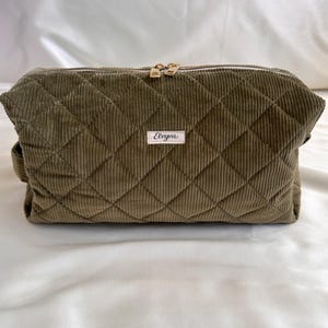 May include: Olive green corduroy cosmetic bag with a quilted diamond pattern. The bag has a gold zipper and a small label that reads "Elviva". The bag is rectangular and has a handle on the side.