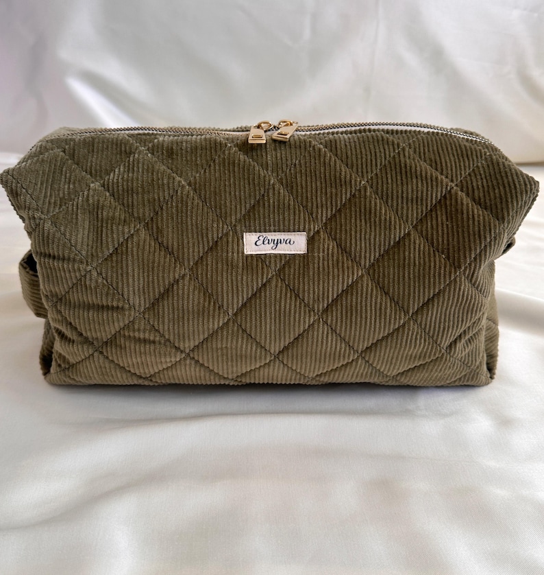 May include: Olive green corduroy cosmetic bag with a quilted diamond pattern. The bag has a gold zipper and a small label that reads "Elviva". The bag is rectangular and has a handle on the side.