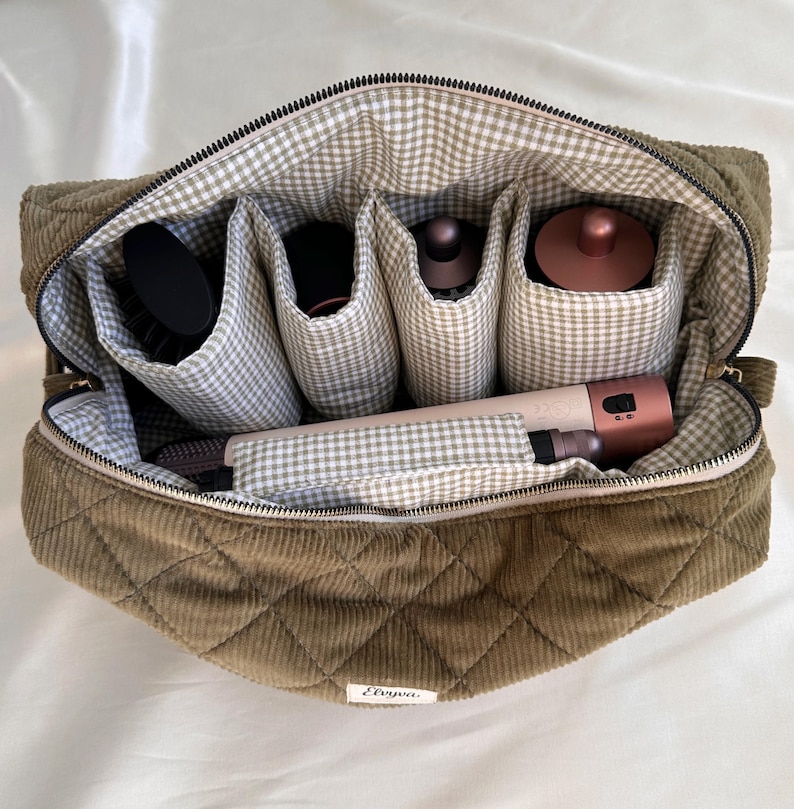 May include: Olive green quilted corduroy cosmetic bag with a gingham lining and multiple compartments. The bag is open, revealing various beauty tools, including a brush and hair styling tools.