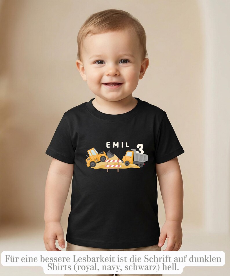 May include: A black short-sleeved t-shirt featuring a graphic of a yellow construction excavator and a dump truck on a pile of dirt. The text EMIL is printed in white above the vehicles, with the number 3 displayed in white to the right side.