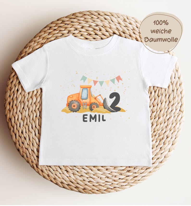 K&ouml;nnte beinhalten: Ein wei&szlig;es Kurzarm-T-Shirt mit einer Grafik eines orangefarbenen Baggers, der schwarzen Zahl 2 und dem Namen EMIL in dunkelgrauen Buchstaben. &Uuml;ber dem Bagger befinden sich bunte dreieckige Wimpel und goldene Sprenkel.