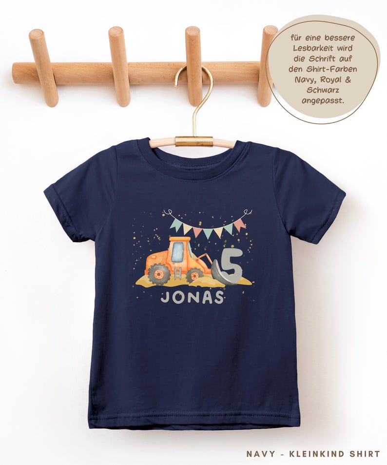 K&ouml;nnte beinhalten: Ein marineblaues Kurzarm-T-Shirt mit einer Grafik eines orangefarbenen Baustellentraktors, einer gro&szlig;en grauen Zahl 5 und dem Namen JONAS in wei&szlig;er Schrift. &Uuml;ber dem Traktor befindet sich eine Girlande aus bunten Wimpeln.