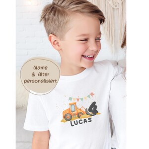 K&ouml;nnte beinhalten: Ein wei&szlig;es T-Shirt mit kurzen &Auml;rmeln, das mit einer Grafik eines orangefarbenen Baggers, der schwarzen Zahl 4 und dem Namen LUCAS in schwarzer Schrift bedruckt ist. &Uuml;ber dem Bagger befindet sich eine bunte Wimpelkette.